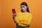 Doubtful uncertain beautiful woman wearing yellow sweater while using smartphone device