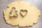 Dough with blanks of cookies in the shape of one gingerbread man and a heart on a gray kitchen table