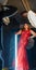 Drag queen posing with bright long lamp in a hand in red shiny dress. A wig with red long hair and make up