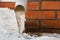 Drain pipe with frozen stream of water near house brick wall