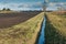 Drainage channel running alongside a ploughed field
