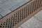 A drainage ditch covered with an iron patterned lattice on a sidewalk made of granite tiles.