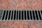 Drainage grate with iron stripes on the walkway with a red stone granite.