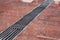 Drainage grate with stripes on the floor with a wet red stone granite surface.