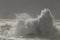 Dramatic beach scene at sunset featuring turbulent waves crashing against rocks and sandy shoreline