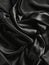Dramatic black satin folds and curves create an abstract composition showcasing the rich sheen and shadowy depths of the