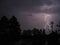 A dramatic bolt of branching lightning silhouettes foreground trees.