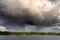 Dramatic clouds from which it rains, over a blue lake with a green strip of forest on the shore