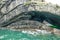 Dramatic coastal cliff rock layers curve, forming cave in teal aqua ocean waves on Loop Head Peninsula, County Clare, Ireland.