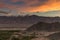 Dramatic colorful sunset with mountains cover with snow and small city below Dramatic overcast sky