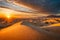 A dramatic desert landscape with rolling sand dunes under a blazing sunset sky