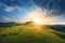 This dramatic Easter Morning Sunrise panorama with blue sky, bright clouds, sunbeams, and large cross on a grass covered hill