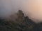 Dramatic fog among giant rocky mountains. Ghostly atmospheric view to big cliff in cloudy sky. Low clouds and beautiful rockies.