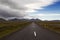 Dramatic Icelandic landscape. Dark asphalt road perspective with wild empty field and mountain range background