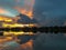 Dramatic light and dark sunset reflecting over calm tree-lined lake after a storm