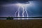 Dramatic lightning bolts over field and serene lake backdrop