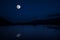 This dramatic moon rise in a deep blue night time sky is accented by highlighted clouds and beautiful, calm lake reflection.