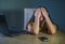 Dramatic portrait of young sad and scared woman covering face with hands stressed and worried looking at laptop computer isolated