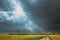 Dramatic Rain Sky With Rain Clouds On Horizon Above Rural Landscape Camola Colza Rapeseed Field. Country Road