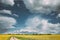 Dramatic Rain Sky With Rain Clouds On Horizon Above Rural Landscape Camola Colza Rapeseed Field. Country Road