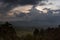 Dramatic rainy dark sky on sunset - heavy blue clouds and shining orange, yellow sunbeams after rain over smoky tropical valley.