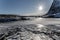 Dramatic Scandinavian winter landscape with frozen lake, mountains, rack for drying fish and rorbu at Lofoten Islands, Norway.