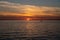 Dramatic sunset over the ocean while the silhouette of a boat and the nuclear power plant is visible on the horizon