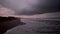 Dramatic view of dark ocean shore under stormclouds at dawn. First ligh on a beach with white foam of waves rolling on