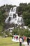 Dramatic waterfall Tvindfossen in Norway with tourists walking up path.