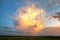 Dramatic yellow sunset over rural area with stormy puffy clouds lit by orange setting sun and blue sky