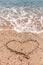 Drawing of a heart on the sand on the beach and wave with foam. Sea travel and holiday.
