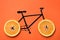 Drawn bicycle with orange slices instead of wheels on coral background, top view