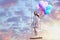 Dream world. Young woman with bright balloons on swing in sunset sky