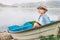 Dreaming boy with book sits in old boat on the mountain lake ban