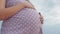 Dreaming pregnant woman in field on background of beautiful clouds