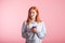 Dreaming redhead girl with phone in studio on pink background.