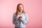 Dreaming redhead girl with phone in studio on pink background.