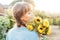 Dreaming young female farmer woman with closed eyes holding and sniffing a sunflowers bouquet on the green garden