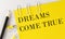 DREAMS COME TRUE word on the yellow paper with office tools on white background