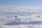 Dreamy aerial view of snowcapped alpine mountain range peaking through heavy clouds