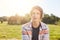 Dreamy attractive boy with light hair, dark eyes and thin lips wearing shirt sitting over green nature background looking aside wi