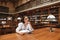 Dreamy beautiful woman sitting in a public library with a book and looks away. Studying in the library