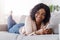Dreamy black girl lying on couch and messaging on smartphone at home