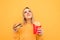 Dreamy blond girl is standing on a yellow background with harmful food in her hands, holds a burger and French fries, looks up and