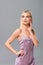 Dreamy blonde girl in violet satin dress posing  on grey