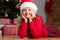 A dreamy child lies on the floor against the background of a Christmas tree. Little girl in a santa hat