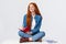 Dreamy and creative cute diligent female student with red hair, in glasses, sitting on floor with legs crossed