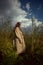 Dreamy gentle woman in a beige raincoat in nature. Romantic young woman in thick tall grass in field. Natural beauty, enjoyment of