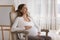 Dreamy pregnant woman sit on armchair smile staring into distance