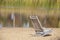 Dreamy scene of wooden beach chair in sand with reflections of reeds in water and willow branches on side - selective focus